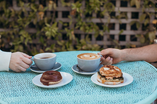 close up of two hands on their own craft coffee beverage with baked goods sitting beside on a cafe table