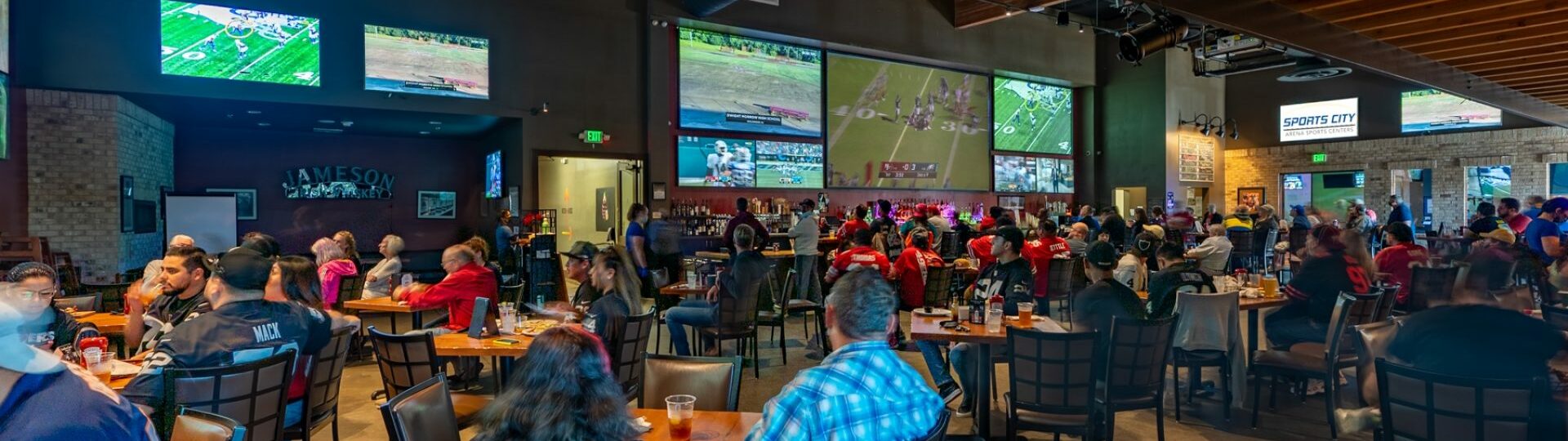restaurant and pub with people eating, drinking, and watching sports from several television screens