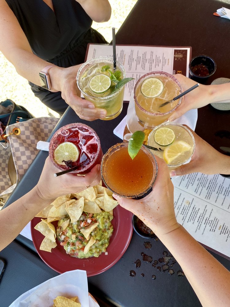 close up of people clinking five cocktail glasses with chips and guacamole on the table below