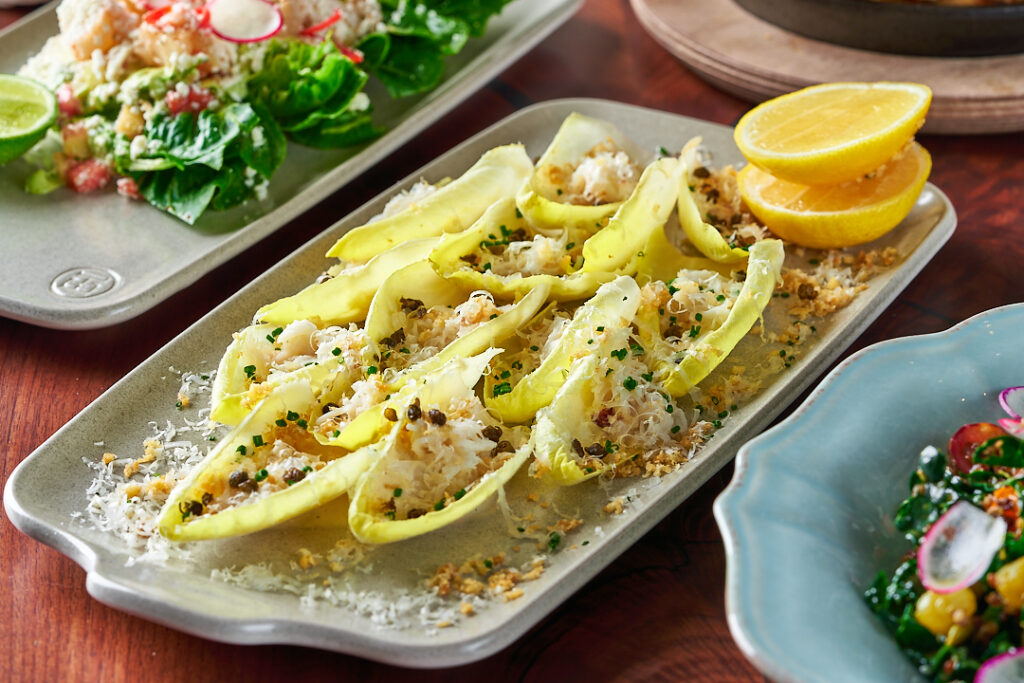 romaine hearts appetizer filled with grated cheeses, ground pepper, and herbs with lemon slices on the slide.