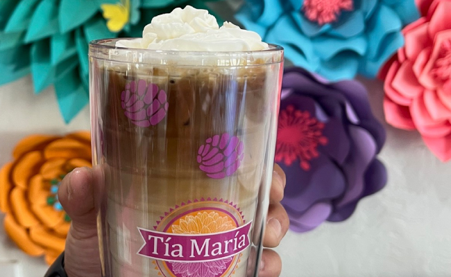 Tia Maria horchata latte with whip cream being held in front of an artificial decorative flower wall.