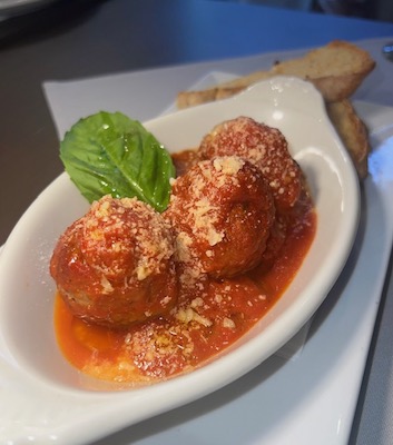 L'Oro Di Napoli meatballs covered in marinara with parmesan cheese and a basil leaf.