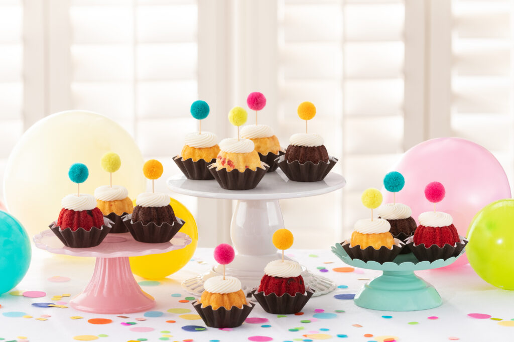 Nothing Bundt Cakes. Mini bundt cakes with frosting arrange on a table with poms, confetti, and balloons.