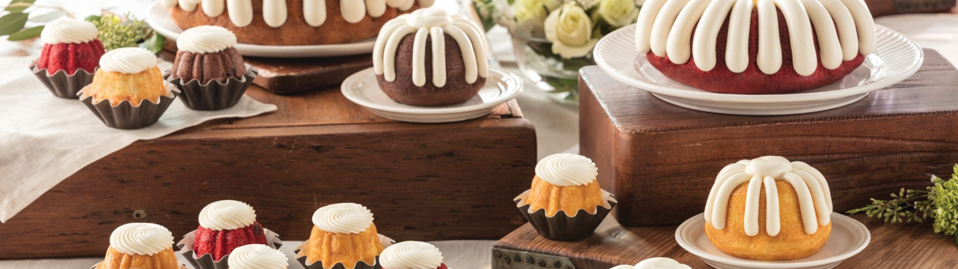 Nothing Bundt Cakes. Large and mini bundt cakes arrange on a table with icing and flower decor.